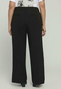 Pantalones de pierna ancha negros con dos bolsillos traseros, tejido suave y un diseño ajustado que llega hasta los tobillos.