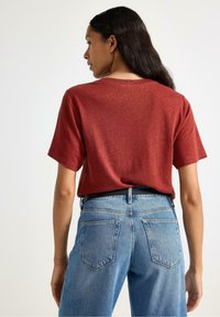 Rød kortærmet t-shirt lavet af blødt stof, med en afslappet pasform. Bæres med højtaljede blå jeans med baglommer.