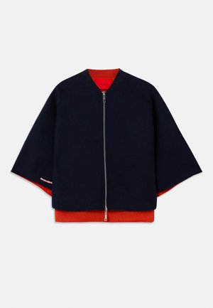 Marineblå zip-jakke med raglanermer, rød innerfôr og kontrasterende rosa sting. Myk tekstur med en avslappet, boxy silhuett.
