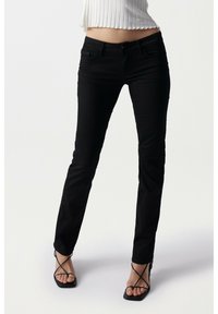 Jeans skinny negros con un ajuste ceñido, hechos de denim. Presentan bolsillos tradicionales, trabillas para cinturón y una cremallera en la bragueta. Textura suave.