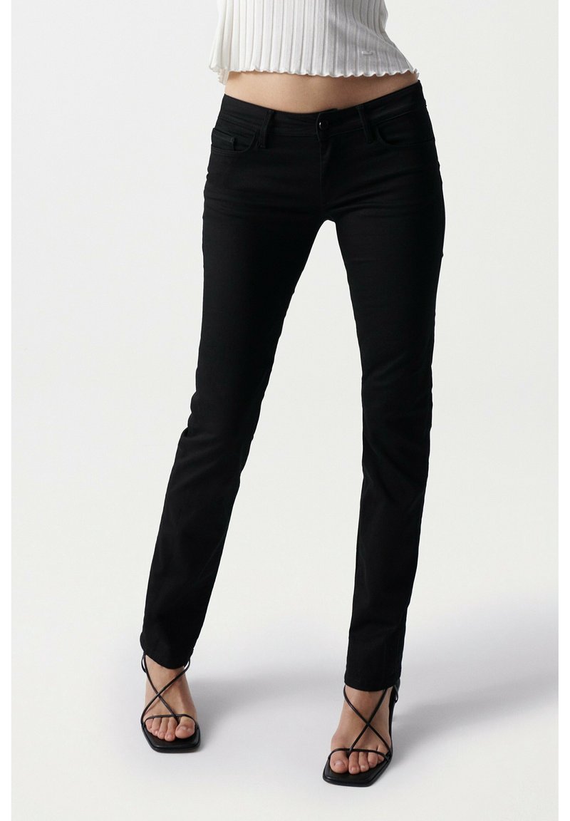 Jeans skinny negros con un ajuste ceñido, hechos de denim. Presentan bolsillos tradicionales, trabillas para cinturón y una cremallera en la bragueta. Textura suave.