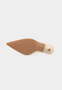 Σόλα παπουτσιού με μυτερή μύτη σε ταμπά χρώμα με τακούνι σε κρεμ απόχρωση και τετράγωνο τελείωμα τακουνιού, εμφανιζόμενα από κάτω σε λευκό φόντο.