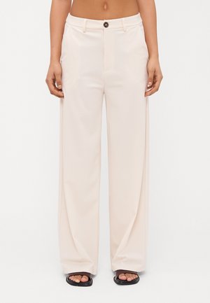 Wide-leg beige trousers with a smooth texture, featuring a button closure and front pockets, paired with black slide sandals.