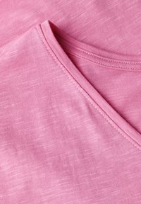 Světle růžová tričková látka s designem V-šálu s texturovaným povrchem a úhledným šitím kolem výstřihu. Měkký a hladký vzhled.