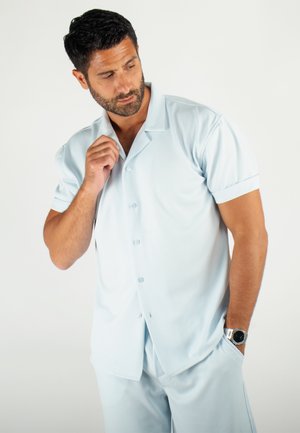 Chemise à boutons à manches courtes bleu clair en tissu texturé, assortie à un pantalon. Dispose d'un col classique et d'une coupe décontractée.