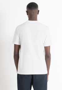 Camiseta de algodón blanca con mangas cortas y cuello redondo, vista desde la parte posterior. La camiseta tiene una textura suave y un ajuste relajado.