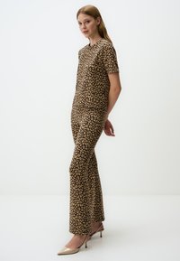 Leopardprint twee-delig outfit in bruin tinten, met korte mouwen en uitlopende broeken. Gekleed met beige puntschoenen.