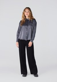 Grijze lange mouwen shirt met een voorkantzak en logo print, gecombineerd met zwarte wijde broek en chunky zwarte schoenen. Zachte stof textuur.