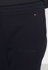 Granatowe spodnie dresowe z elastycznym pasem, bocznymi kieszeniami oraz wyszywanym logo "Tommy Hilfiger" w dopasowanym kolorze. Miękka faktura tkaniny.