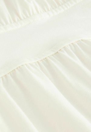 Svetlý slonovinový textil so hladkým povrchom, s naberaným dizajnom v dolnej časti a plochým, elastickým pásom na vrchu.