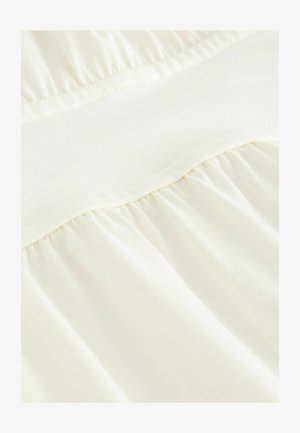 Tissu ivoire clair avec une texture lisse, présentant un design froncé sur la partie inférieure et une taille plate élastiquée en haut.