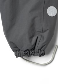 Sivý vodeodolný materiál bundy s nariaseným lemom a nastaviteľným sťahovacím šnúrkou. Obsahuje kruhovú sivú nášivku s logom na rukáve.