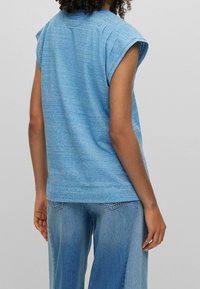 Modrý melírovaný top bez rukávů s uvolněným střihem, kulatým výstřihem a jemnými švy, spárovaný s světle modrými širokými džínami.