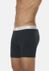 Boxer-briefs noirs avec une ceinture élastique beige ornée d'accents du logo Adidas blanc, fabriqués en tissu lisse et extensible.