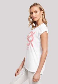 Weißes T-Shirt mit kurzen Ärmeln und einem roten Blättermuster auf der Vorderseite. Der Stoff wirkt weich, hat eine lockere Passform und einen abgerundeten Saum.