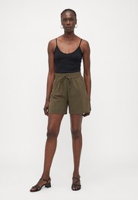 Black fitted camisole top, olive green linen shorts with waistband drawstring, and black strappy sandals. Clear background.