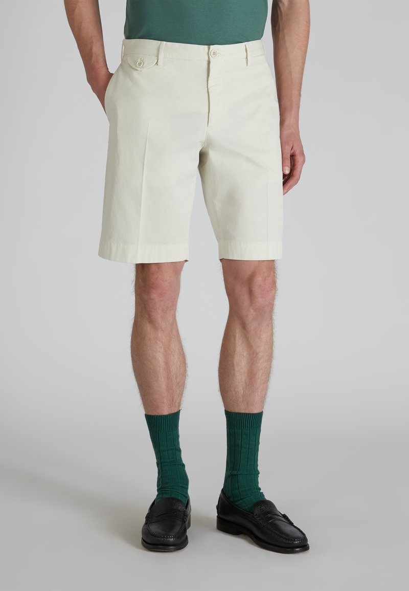 Shorts in cotone beige chiaro con pieghe, dotati di tasche laterali e un orlo pulito. Abbinati a calze verdi a costine e scarpe nere.