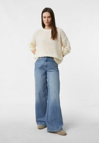Kremowy sweter z dzianiny o luźnym kroju, połączony z szerokimi, jasnoniebieskimi jeansami. Charakterystyczne luźne rękawy i wysoki stan.