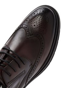 Zapato de vestir de cuero marrón con detalles de brogue clásicos, puntera redondeada y cordones negros, con una superficie texturizada y un acabado suave.