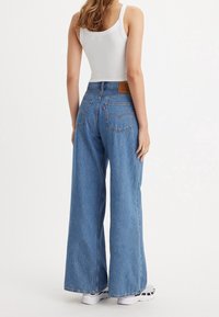 Ljusblå, vida jeans med hög midja och bakfickor, tillsammans med en vit linne och vita sneakers. Texturerad denimfinish.