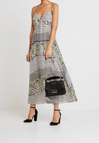 Maxiklänning med svartvita geometriska mönster och gröna djurtryck. Svart handväska med silverdetaljer, matchad med svarta klackar.