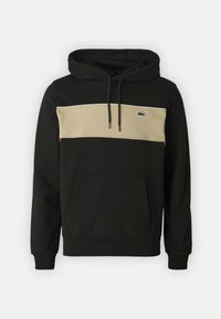 Sweat à capuche noir avec une bande horizontale beige et une poche kangourou. Caractéristiques : cordons de serrage et un petit logo vert sur la poitrine. Tissu doux.
