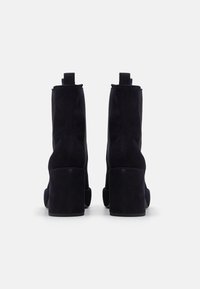 Bottines en suede noir avec un talon carré, présentant une surface texturée et des languettes à l'arrière pour un enfilage facile.