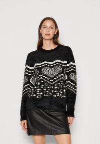 Maglione fuzzy bianco e nero a fantasia con scollo rotondo e polsini a coste, abbinato a una gonna di pelle nera.