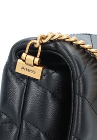 Borsa a mano in pelle nera con texture trapuntata, hardware in tono oro e tracolla a catena. Presenta un'etichetta del marchio ben visibile con la scritta "PINKO."