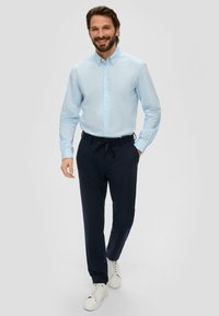 Lichtblauw overhemd met subtiele strepen, gecombineerd met marineblauwe broek en witte sneakers, wat een relaxte pasvorm en casual stijl presenteert.