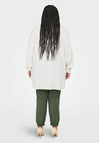 Chemise blanche oversize en tissu texturé, associée à un pantalon vert olive cintré et à des talons beiges, vue de dos.