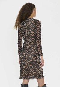 Durchsichtiges Kleid mit einem Tigerstreifenmuster in Schwarz und Beige, langen Ärmeln und einer knielangen Saumlinie. Glatte Textur, figurbetonte Silhouette.