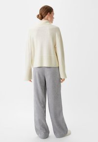 Cremiger Strickpullover mit hohem Kragen, kombiniert mit grauen gestreiften weit geschnittenen Hosen. Beide Kleidungsstücke zeichnen sich durch weiche Texturen und eine lässige Passform aus.