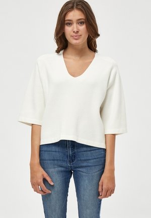 White V-neck cropped sweater with wide sleeves, made of textured fabric, paired with blue denim jeans. Simple and clean design.