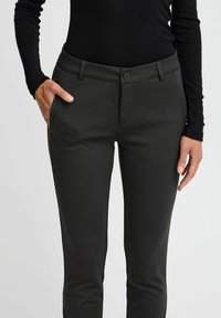Pantaloni grigi scuri su misura con una texture liscia, dotati di tasche laterali e chiusura frontale a bottone. Fit slim con un design moderno.