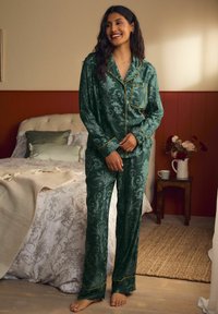 Zelený saténový pyžamový set s kvetinovým vzorom, zlatým lemovaním na golieri a manžetách, uvoľnený strih, dlhé rukávy a zodpovedajúce nohavice.