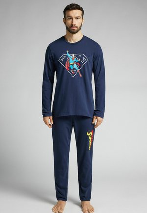 Navyblaues Langarm-Pyjama-Set mit einem Superman-Motiv auf dem Shirt und "Superman"-Text in Rot und Gelb auf den Hosen. Weiches Material.