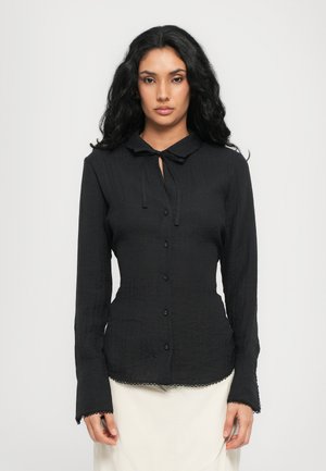 Zwarte blouse met knopen en een kraag, detail met stropdas, textuurstof en uitlopende mouwen met golvende randen. Eenvoudig en goed passende ontwerp.