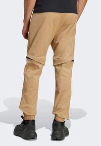 Beige nylon trousers with elastic cuffs and zippered side pockets, featuring a relaxed fit and a slightly shiny texture. Black footwear.