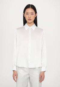 Witte lange mouwen blouse met een klassieke kraag, knoopsluiting aan de voorkant en een gladde textuur. Gecombineerd met glanzende zilveren broeken voor contrast.