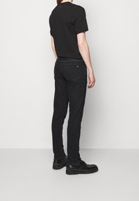 Camiseta negra de manga corta combinada con jeans negros ajustados. Los jeans tienen bolsillos y un sutil detalle de logo en la parte trasera.