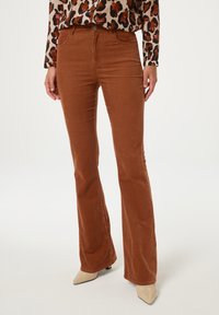 Bruin corduroy flared broek met voorzakken en een knoopsluiting, gecombineerd met een gestreepte lange mouwen top en puntige beige hakken.