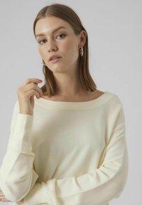 Cremfarbener, gerippter Pullover mit schulterfreiem Ausschnitt und langen Ärmeln; weicher Stoff und lockere Passform.