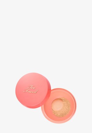 Runder korallenfarbener Make-up-Behälter mit goldenem "Too Faced"-Text und losem beigem Puder darin auf weißem Hintergrund.