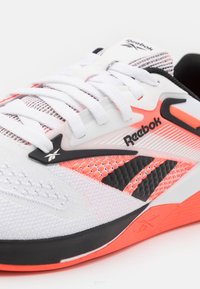 Baskets Reebok blanches et orange néon avec des accents noirs, dessus en mesh, lacets blancs et logo de la marque sur le côté et la languette.