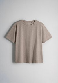 Beige short-sleeve cotton t-shirt with crew neck, hanging against a plain light gray wall.