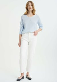 Lichtblauwe gebreide trui met een v-hals en drie knopen, gecombineerd met slim-fit witte jeans en zwarte ballerina's.