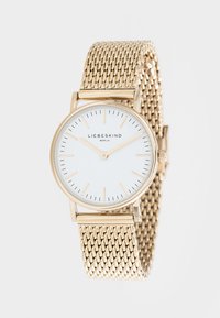 Gouden mesh band horloge met een ronde witte wijzerplaat, minimalistische gouden uurmarkeringen en een centraal logo. Elegant en modern ontwerp.