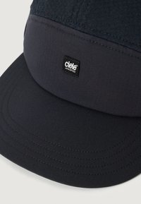 Gorra azul marino con un panel superior texturizado y una visera lisa, con una pequeña etiqueta negra que muestra el logo de "Ciele Athletics".