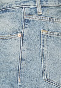 Jeans de mezclilla azul claro con una textura desgastada, que cuentan con dos bolsillos traseros, costuras doradas y un detalle de remaches en oro rosa.